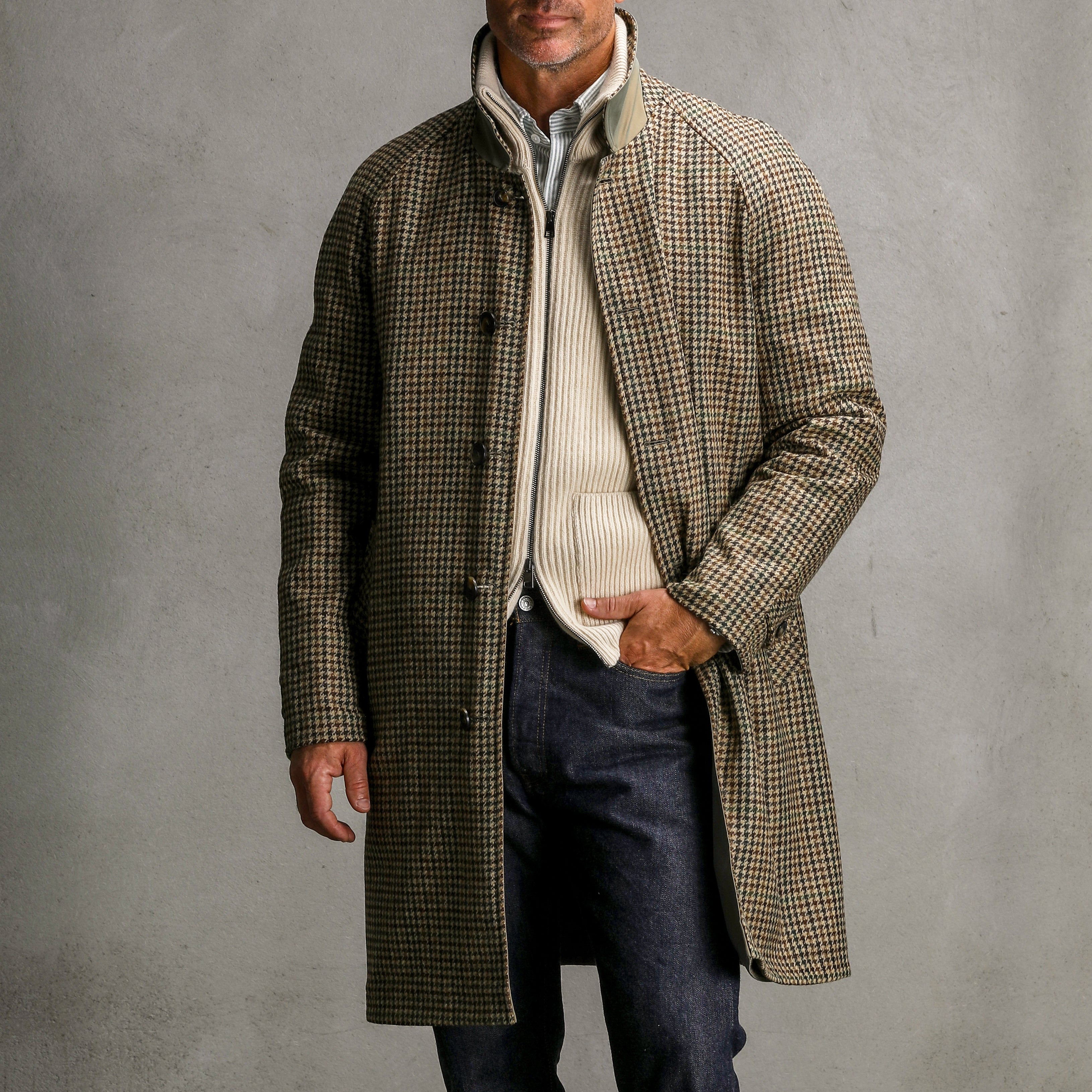 A person wearing a long, checked overcoat over a G.R.P Ecru Beige Wool Cashmere Knitted Jacket and a collared shirt with dark pants stands in front of a plain background.