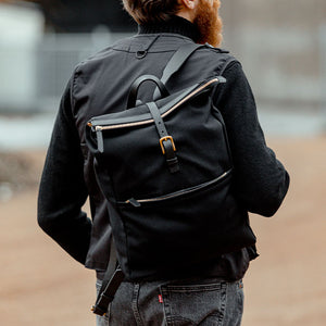 A man with a Mismo Coal Black M/S Nylon Express Backpack walking down the street.