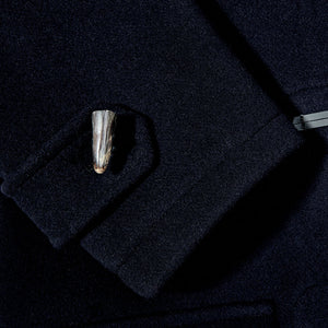 A close up of a silver cufflink on a Gloverall Navy Blue Wool Morris Duffle Coat.