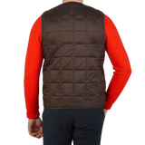 The back view of a man wearing a Taion Dark Chocolate Nylon Down Padded Vest and orange sweater.